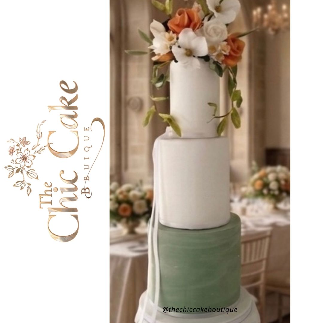 Tall statuesque tiered wedding cake featuring a sage green marbled bottom tier, smooth white top tiers, and a vibrant orange and white sugar floral topper inside a grand castle banquet hall. This sage green and orange wedding cake made by the chic cake boutique serving Munster Ireland